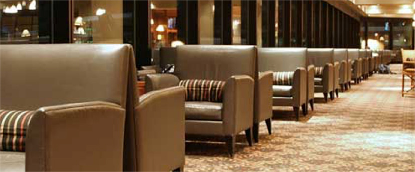 A large hotel lobby, with empty brown leather upholstered armchairs positioned back-to-back in pairs in a row of over ten sets.